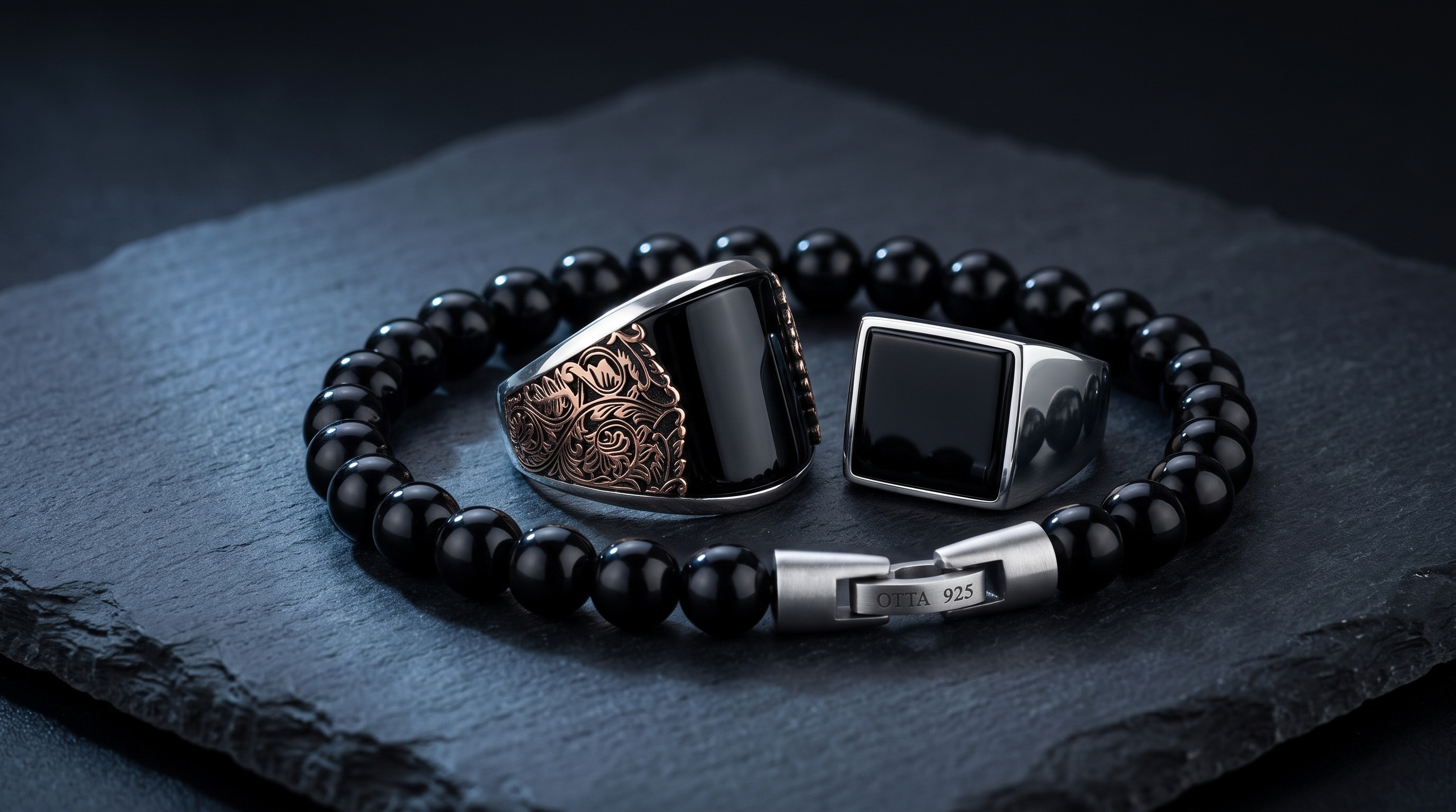 Engraved silver black onyx ring and square onyx signet inside a black onyx bead bracelet on slate