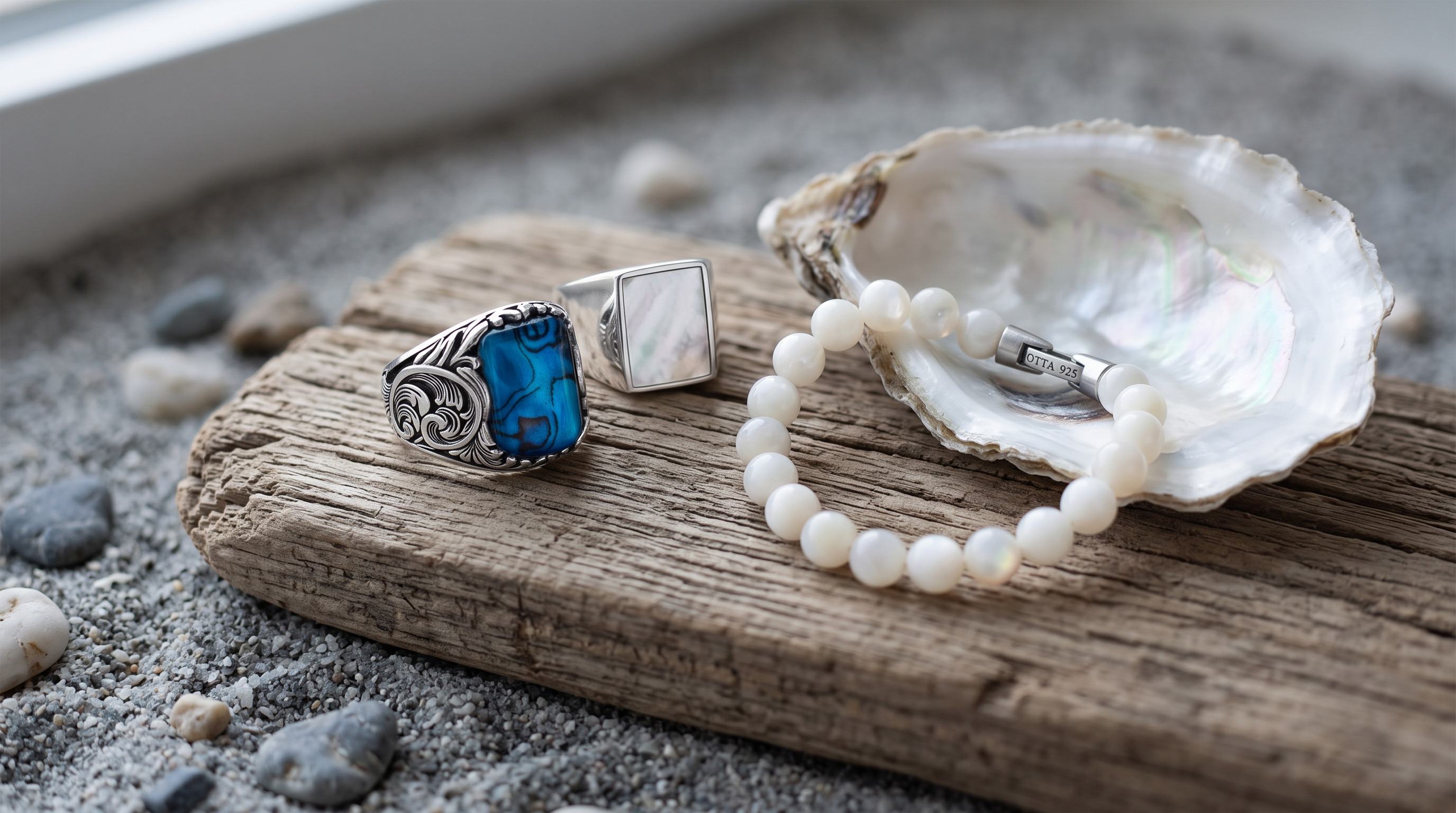 Engraved silver ring with blue mother of pearl, a white mother of pearl signet and a mother of pearl bead bracelet beside an open oyster shell